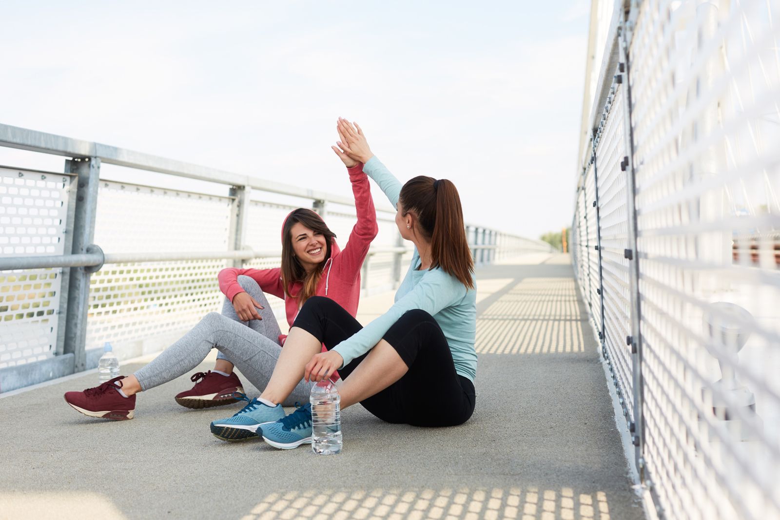 Two friends high-fiving on a bridge after a run