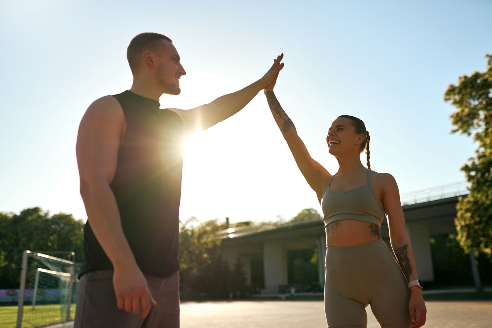 Two people high-fiving and laughing after an outdoor workout in the sun
